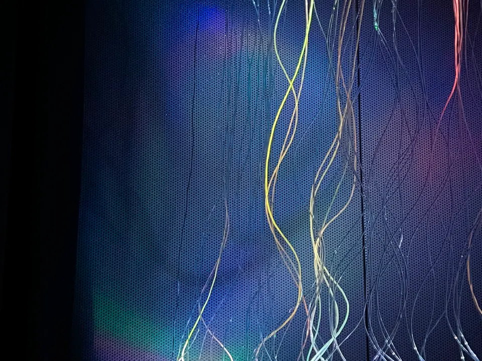 Curving illuminated strands against a dark background, with blue, green, and pink light
